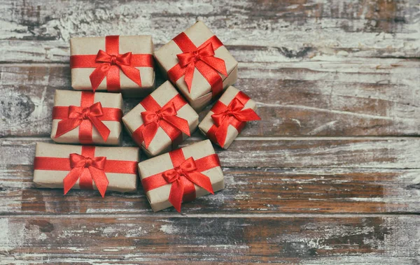 茶色のクラフトペーパーに包まれたギフトボックスと赤いサタンのリボンを結ぶギフトボックス 装飾的な木製の背景 テキストスペース プレゼントのセット — ストック写真