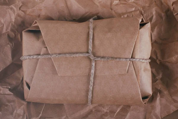 Parcel package wrapped with brown craft paper tied rope. Boxing process. Crumpled paper texture background.