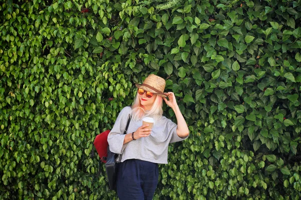 Yaz zamanı. Yeşil duvar arka plan üzerinde kahve, açık pembe saç, hasır şapka ve sırt çantası ile genç kız.