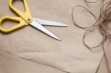 Paketleme işlemi. Sunar sarma. Sarı makas, kurdeleler, kenevir dizeleri ve konuları, kahverengi zanaat kağıt doku arka plan. Hediyelik eşya dükkanı. 