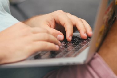 Dizüstü bilgisayar klavyesi üzerinde yazan genç bir adam. Yakın çekim detayları. İnsan elleri. İnternette çalışıyorum. Serbest kavram. Kanepede alışveriş yapın. Online alışveriş.