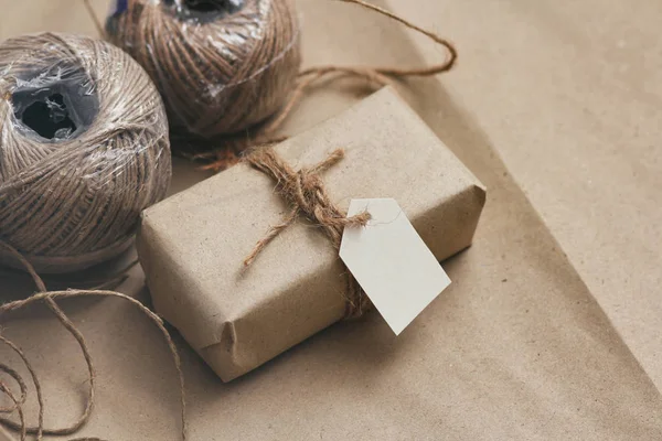 Parcel wrapping in brown craft paper and tie hemp string. Package with paper label. Delivery service. Online shopping. Your purchase. Gift box on a table. Hemp threads.