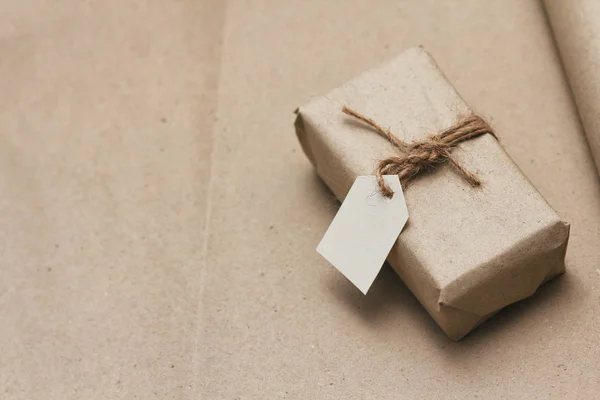 Paket kahverengi el işi kağıdıyla sarılıp kenevir ipliğine bağlanmış. Kağıt etiketli paket. Teslimat servisi. İnternetten alışveriş. Satın alın. Hediye kutusu masanın üstünde. Kenevir iplikleri.