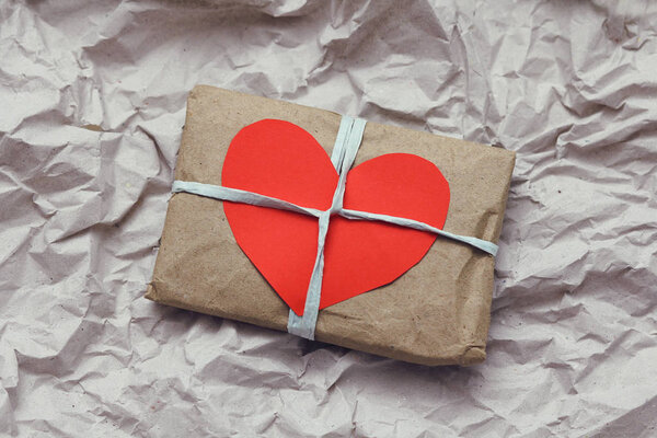 Мягкая сумка, завернутая в бумагу и шнур для галстука. Большая открытка с красным картонным сердцем. Смятая бумажная текстура фона. Служба доставки. Интернет-магазины
.