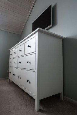 Komodinin üzerinde mobilya ayak üzerinde çekmeceli beyaz çekmeceli bir flat Tv olduğunu