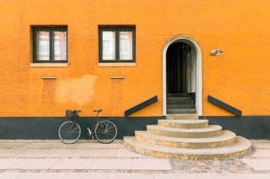 Black bicycle near orange-yellow wall of the old residential building in Copenhagen, Denmark clipart