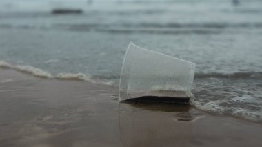 Plajda terk edilmiş, tek kullanımlık plastik bardak. Denizi kirleten gelgit tarafından sürüklenir.