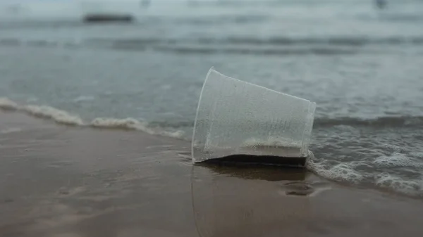 可处置的透明塑料杯被遗弃在海滩上 被潮水拖走 弄脏了大海 — 图库照片