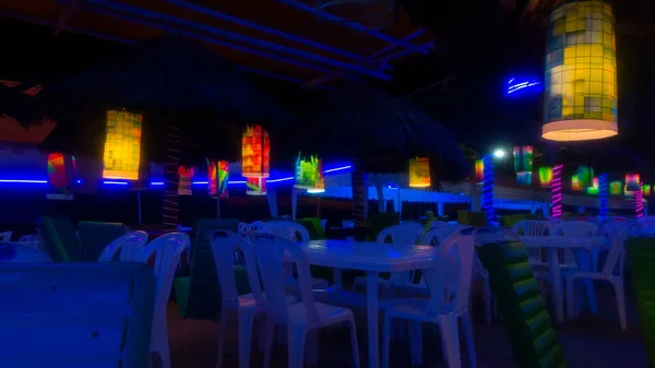 Plastic tables inside an empty disco bar with blue lights near the beach