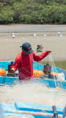 Palmar, Santa Elena / Ekvador - 19 Ekim 2019: Sanatçı balıkçı arka planda kuşlarla birlikte nehrin kenarındaki teknesinde ağını dikiyor
