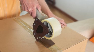 Karton bir kutuyu yapışkan bantla kapatan bir kadının ellerine yaklaş.