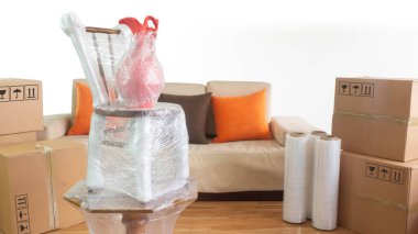 Koltuk, plastik rulo ve beyaz arka planda kapalı karton kutular olan bir odanın içinde plastik bir masa üzerinde vazo ile hareket sahnesi.