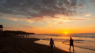Mancora, Piura / Peru - 7 Nisan 2019: Güneş deniz ufkunda saklanırken gün batımında sahilde yürüyen turistler