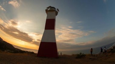 Mancora, Piura / Peru - 9 Nisan 2019: Mancora deniz fenerinin yanındaki turistler bulutlu bir günbatımında dağın üzerinde