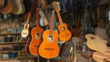 Gitar atölyesinin genel görünümü, ahşap gitarlar ve arka duvarı aletlerle dolu olan marangozluk masasında birleştirilmemiş pek çok parça.