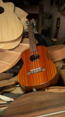 Bir atölyedeki ahşap çalışma masasında birleştirilmemiş gitar parçaları yığını üzerinde kırmızı ahşap gitar.