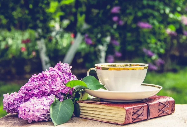 Book, cup of tea and lilac. Fragrant tea in the garden. Romantic concept. Vintage toting