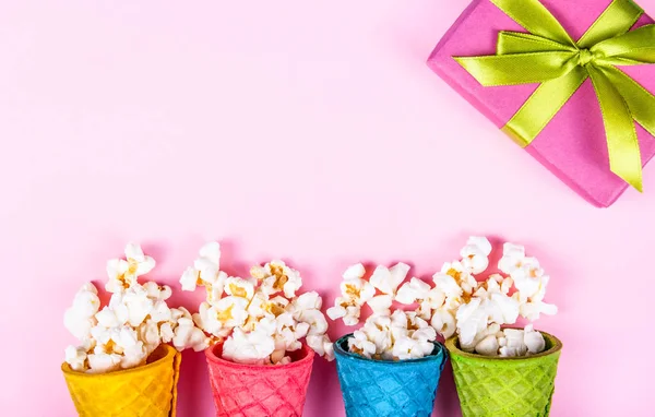 Pink paper background. Pink gift box and popcorn. Colored waffle cones on pink background. Copy space. Top view