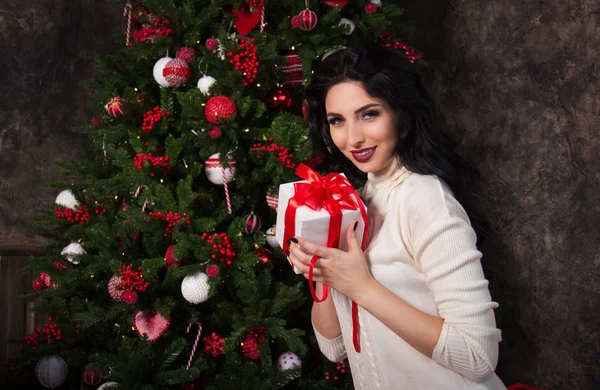 Beautiful young woman with gift and Christmas tree. Beautiful happy woman and new year gift.