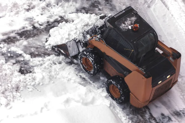 A small urban snow removal machine works in the courtyard of a residential building. View from above. Selective focus.