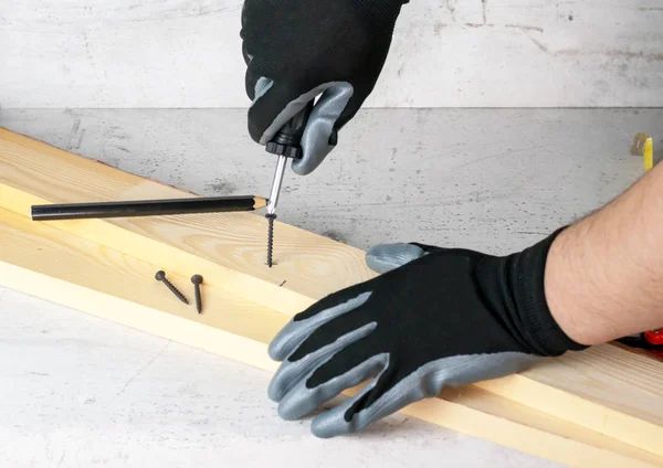 A man puts marks on wooden bars for further screwing in of the screws. Diy at home concept