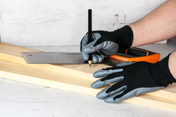 A man puts marks on the wooden bars with a pencil for further work with a saw. Diy at home concept