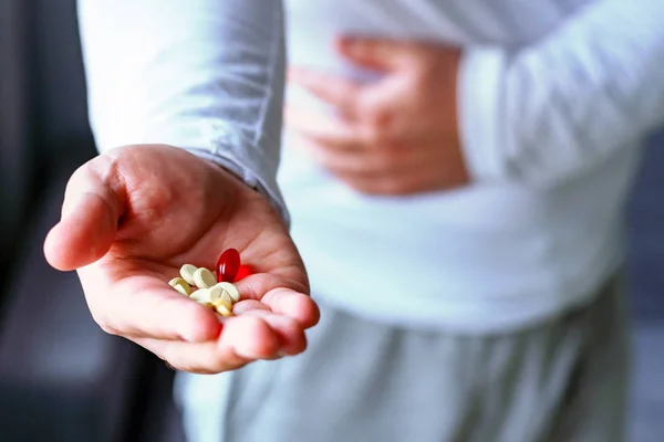 A man holds his stomach, stretches his hand with pills. Health, illness, medicine. Selective focus.