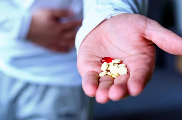 A man holds his stomach, stretches his hand with pills. Health, illness, medicine. Selective focus.
