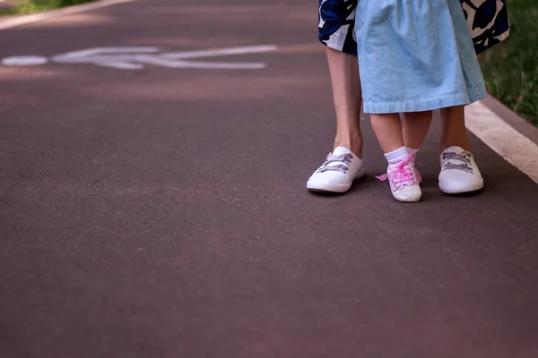 Mom teaches daughter to walk. Summer park, legs closeup. Mom with a one-year-old daughter in dresses are walking in the park. Teaching children, motherhood.