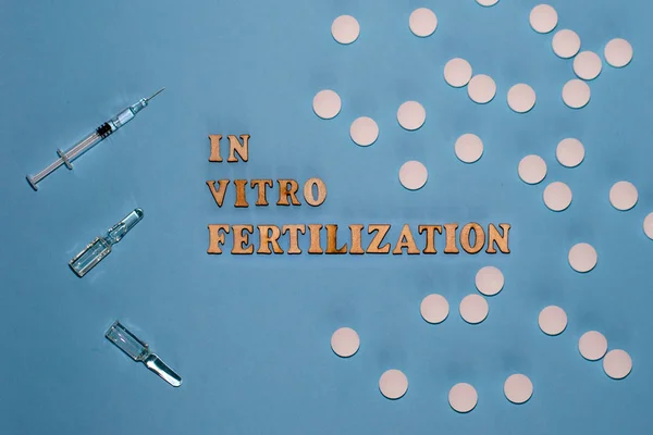 The inscription In Vitro Fertilization is in wooden letters on a blue background. In vitro injection pen ampoule.Infertility.
