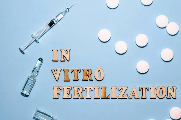The inscription In Vitro Fertilization is in wooden letters on a blue background. In vitro injection pen, tablet and ampoule.