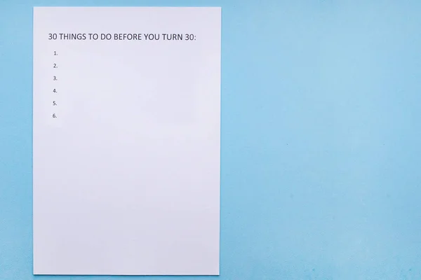 Caption 30 THINGS TO DO BEFORE YOU TURN 30 on white sheet. White sheet on a blue background. Life goals. Goal setting
