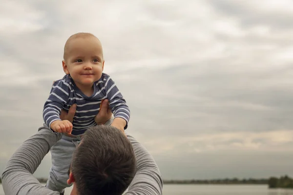 The child is in the arms of his father. A child against the background of the sky in the hands of dad. Happy moments of life.