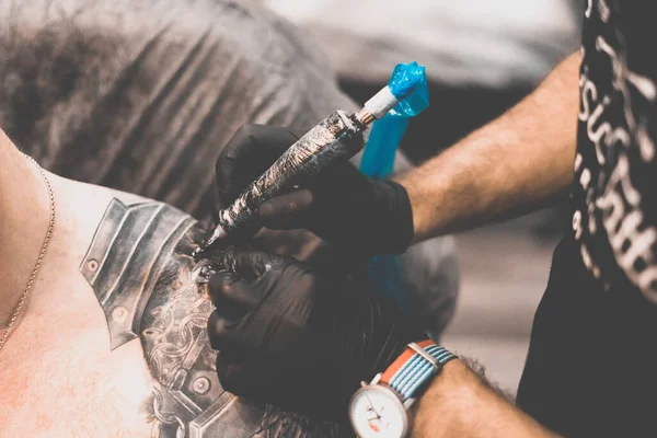 Tattoo salon. The tattoo master is tattooing a man on his shoulder. Tattoo machine, safety and hygiene at work. Close-up, tinted, tattooist