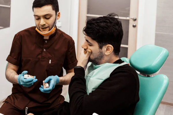 A young dentist discusses a diagnosis and treatment plan with a patient. Discussion and demonstration of treatment results. Health care, aesthetic medicine.