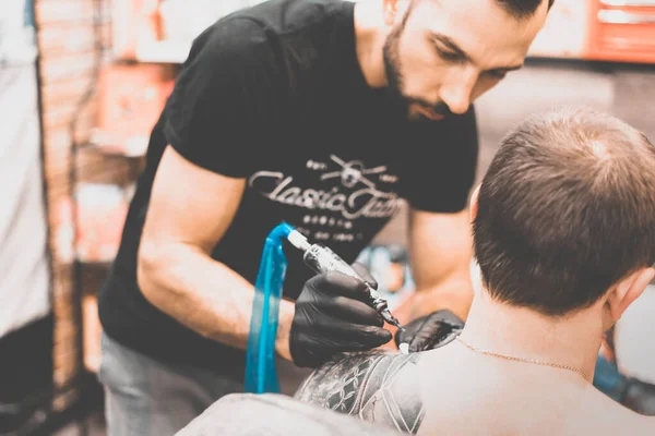 Tattoo salon. The tattoo master is tattooing a man on his shoulder. Tattoo machine, safety and hygiene at work. Close-up, tinted, tattooist