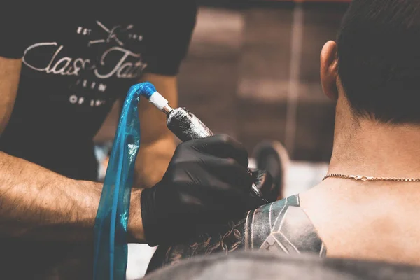 Tattoo salon. The tattoo master is tattooing a man on his shoulder. Tattoo machine, safety and hygiene at work. Close-up, tinted, tattooist