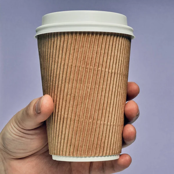 Paper cup in hand on a colored background. Eco-friendly materials in a coffee shop, biodegradable disposable tableware. Close up