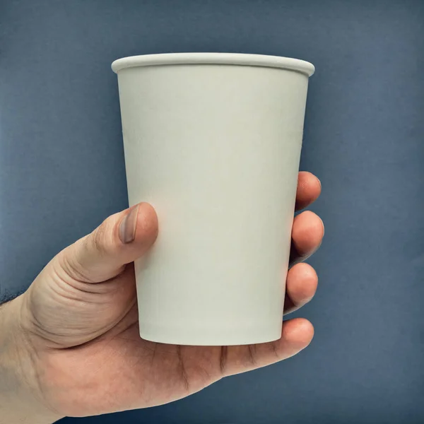 Paper cup in hand on a colored background. Eco-friendly materials in a coffee shop, biodegradable disposable tableware. Close up