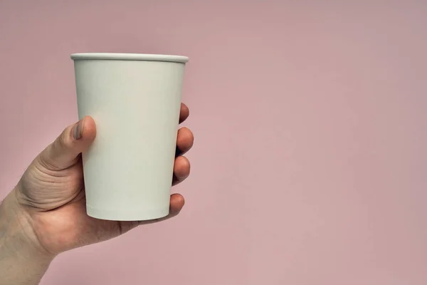 Paper cup in hand on a colored background. Eco-friendly materials in a coffee shop, biodegradable disposable tableware. Close up