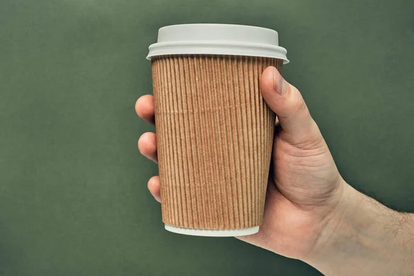 Paper cup in hand on a colored background. Eco-friendly materials in a coffee shop, biodegradable disposable tableware. Close up