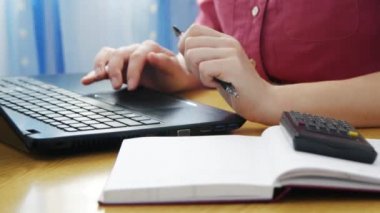 Kız klavyede yazıp not defterine bilgi yazıyor. Konsept evde çalışma, serbest çalışma.