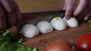 Dilimleme sert haşlanmış yumurta ikiye. Adam mutfakta bıçakla doğrama tahtasında yumurta keser. Salata için kesme malzemeleri. 