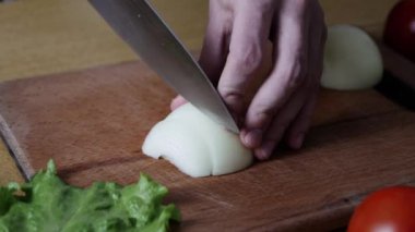 Bir bıçakla soğan keserek pişirin kapatın. Adam yemek yapıyor. Şef soğanı dilimler. Bıçak, kesme tahtası, soğan. Kızartma için eğilin. Salata için sebze kes. Sağlıklı gıda. 