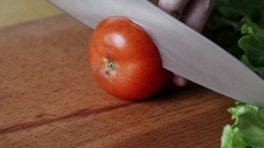 Erkek elleri domates kesiyor. Ahşap bir mutfak tahtasıüzerinde şef bıçağıyla domates leri dilimleyip doğratır. Sağlık beslenmesi, yakın çekim. 