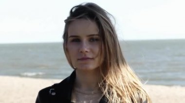 Deniz üzerinde gün batımıbakarak rüzgarda esen sarı saçları ile gülümseyen Genç Kadın yakın portresi. Siyah ceket giyen kız. 