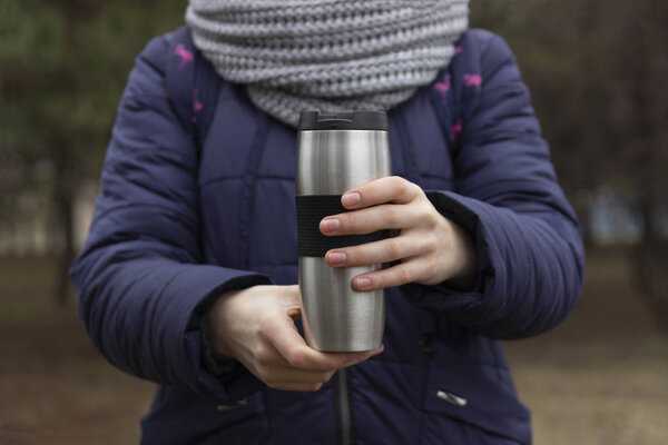 woman hands holding thermo cup of hot coffee on the forest background