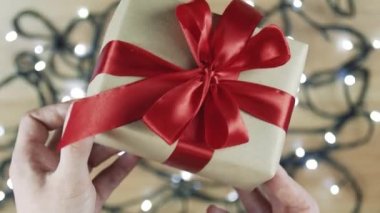 Kadın elleri bir çelenk yanıp sönen bir arka plan üzerinde bir hediye tutan. Düz lay, üst görünüm, yeni yıl.