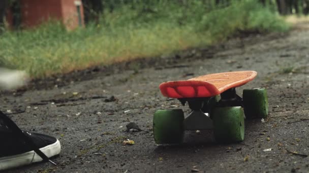 サマーパークでは 男性の足のクローズアップがボードに乗り始めます 屋外の公園でスケートボードに乗るスケーターの少年 オレンジスケートフットウェアシューズ スケートボードデッキ — ストック動画