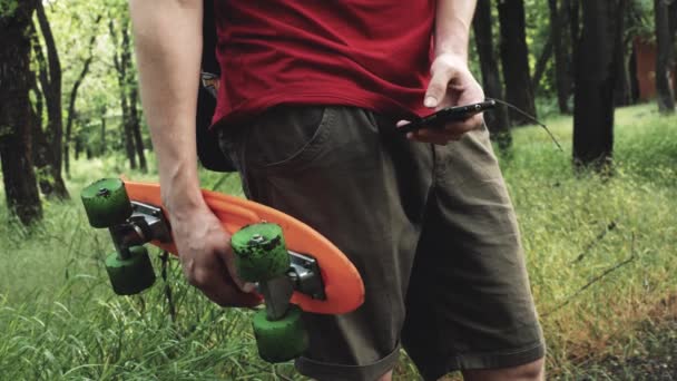 若いですCaucasianヒップスター男とともにスケートボード滞在上の公園とテキストメッセージ上の携帯電話 — ストック動画